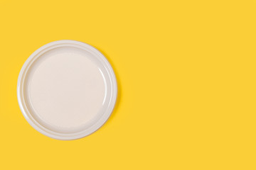 Plato redondo blanco de plástico desechable sobre fondo amarillo liso brillante y aislado. Vista...