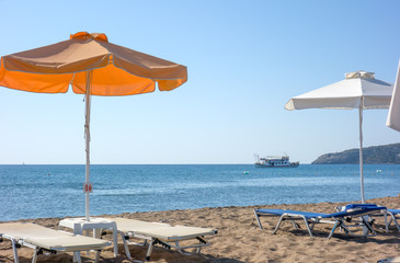 Orange and white umbrella on the sea beach, a pleasure boat sails on the sea.