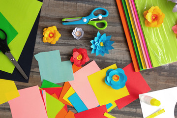 Flat lay of colorful  color paper flowers and scissors on wooden desk. Art studio workplace concept