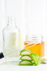 Cosmetic homemade lotion or essential oil from natural sliced aloe vera plant in glass bottles against light grey background.