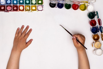 Top view of children's hands while drawing gouache on paper. The child starts drawing a child's drawing.