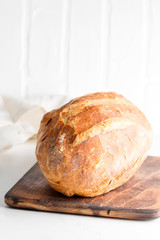 Homemade freshy baked bread on a wooden board and light grey marble table decorated textile towel.