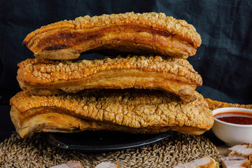 Large crispy pork on a black plate, cut into slices on a wooden chopping board with spicy sauce on a wooden table