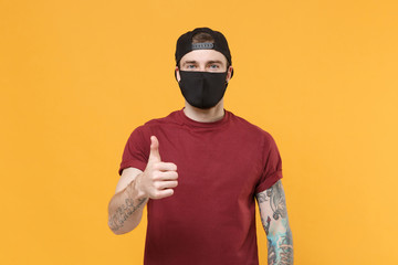 Young tattooed man guy in casual t-shirt cap black face mask posing isolated on yellow wall...