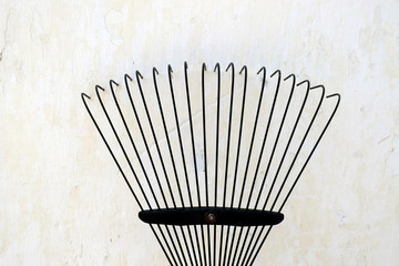 Thin metal rake for harvesting leaves in the garden. Gardening equipment on a background of a whitewashed wall.