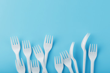 White plastic forks of disposable tableware on a blue background.