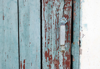 Old wooden door with a metal handle. The door surface is painted blue, peels off over time. Door in the wall with whitewash.