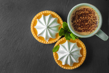 Lemon tart with mint leaves and a cup of cappuccino with chocolate topping