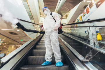 Professional workers in hazmat suits disinfecting indoor of mall, pandemic health risk, coronavirus