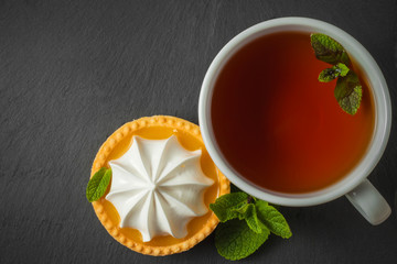 Lemon tart with mint leaves and a cup of tea. Confectionery background on a black slate plate