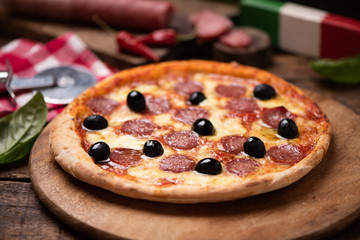 Delicious fresh oven baked spicy salami or pepperoni pizza with melted cheese and olives on a wooden board