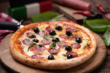 Delicious fresh oven baked spicy salami or pepperoni pizza with melted cheese and olives on a wooden board