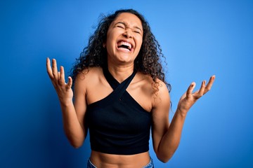 Young beautiful woman with curly hair wearing casual t-shirt standing over blue background...