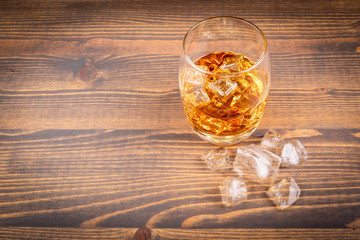 Glass of whiskey and ice cubes on a wooden background