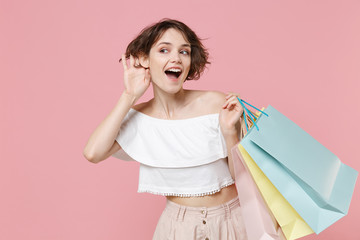 Curious young woman girl in summer clothes hold package bag with purchases isolated on pink...