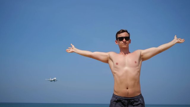 handsome guy with muscular body enjoys sunbathing against approaching over head airplane under blue sky low angle shot