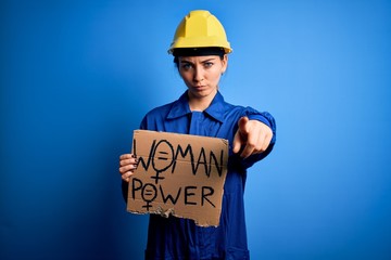 Young blonde worker woman asking for women rights holding banner with power message pointing with finger to the camera and to you, hand sign, positive and confident gesture from the front