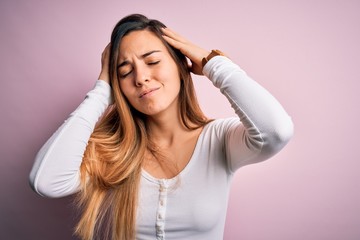 Fototapeta premium Young beautiful blonde woman with blue eyes wearing white t-shirt over pink background suffering from headache desperate and stressed because pain and migraine. Hands on head.