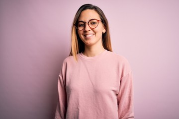 Beautiful blonde woman with blue eyes wearing sweater and glasses over pink background with a happy and cool smile on face. Lucky person.