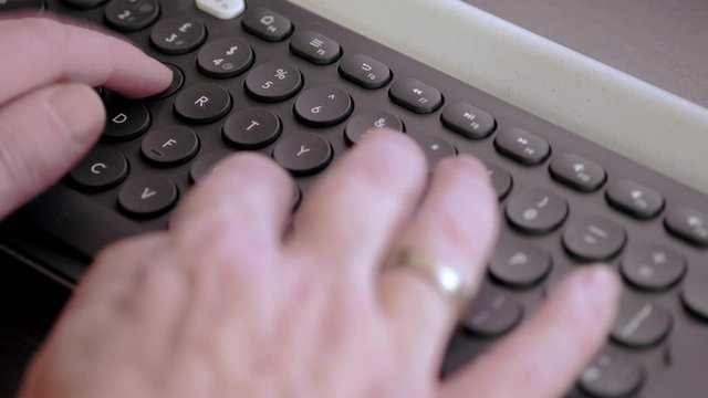 Elevated clip of man's hand typing on black wireless keyboard. 