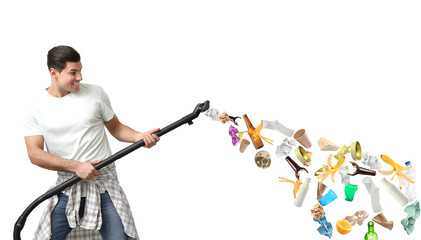 Young man with vacuum cleaner and different garbage on white background