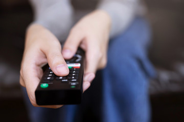 close up Television remote control in casual young female yellow shirt hands pointing to tv set and turning it on or off. select channel watching tv on sofa at home in the living room relax.