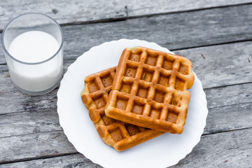 Top view at plate of belgian or viennese waffles with a glass of fresh milk on rustic wooden table
