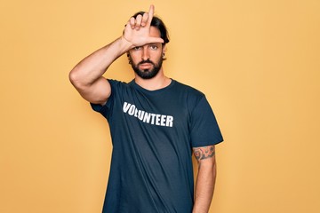 Young handsome hispanic volunteer man wearing volunteering t-shirt as social care making fun of people with fingers on forehead doing loser gesture mocking and insulting.