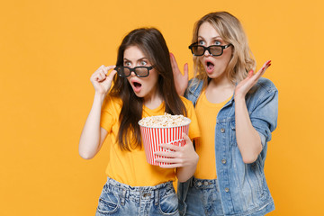 Shocked concerned young women girls friends in denim clothes, 3d glasses isolated on yellow...