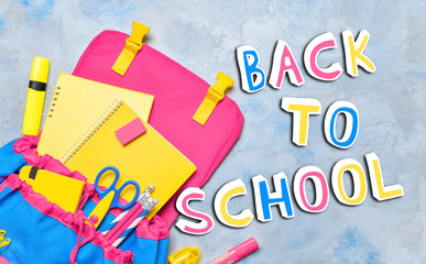 Backpack with stationery and phrase BACK TO SCHOOL on color background