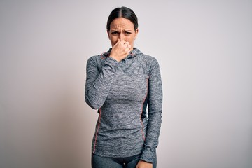 Young blonde fitness woman wearing sport workout clothes over isolated background smelling something stinky and disgusting, intolerable smell, holding breath with fingers on nose. Bad smell - obrazy, fototapety, plakaty