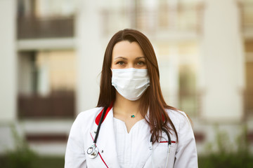 Online webinar or conference concept: Young female doctor in surgical mask and earbuds outdoors