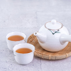 Hot tea in white teapot and cups on a sieve over bright gray cement background, closeup, copy space design concept.