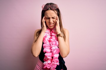Young beautiful blonde woman wearing swimsuit and floral Hawaiian lei over pink background with...