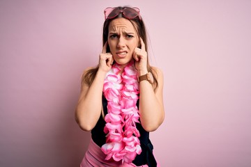 Young beautiful blonde woman wearing swimsuit and floral Hawaiian lei over pink background covering ears with fingers with annoyed expression for the noise of loud music. Deaf concept.