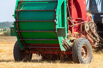 tractor makes big straw roll on yellow field at summer day