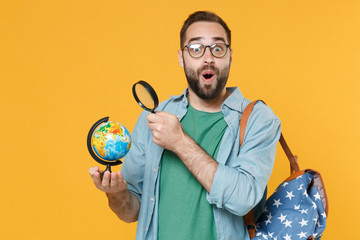 Shocked young man student in casual clothes glasses with backpack isolated on yellow wall background in studio. Education in high school university college concept. Hold world globe, magnifying glass.