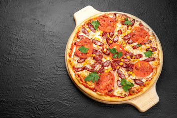 Hunting pizza on a black background, tomato-based with mozzarella, bacon, hunting sausages, parsley, tomatoes and corn