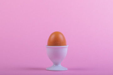 one brown egg in white egg cup before pink background