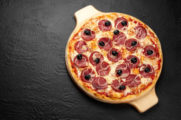 Pizza SALAMI on a black background, tomato-based with mozzarella, salami, onions and olives