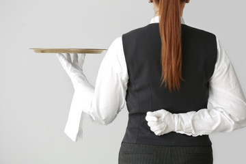 Beautiful female waiter with empty tray on grey background