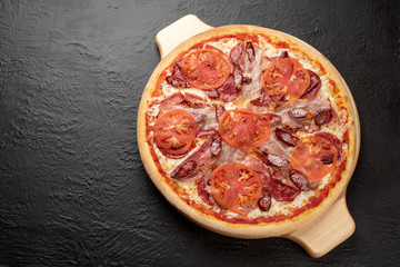 Four-meat pizza on a black background, tomato-based with mozzarella, bacon, ham, salami, hunting sausages and tomatoes