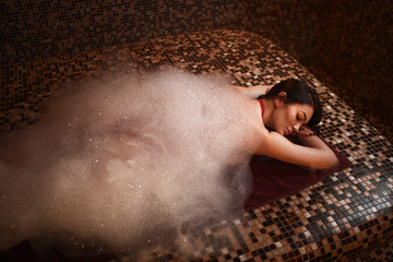 Woman in foam lying on a hot stone in hamam, sauna
