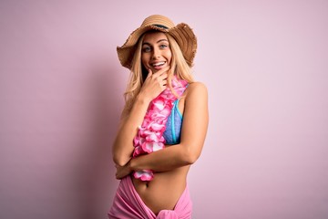 Young beautiful blonde woman on vacation wearing bikini and hat with hawaiian lei flowers looking confident at the camera smiling with crossed arms and hand raised on chin. Thinking positive.
