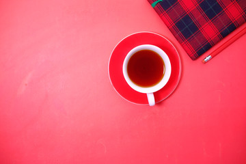 Top view of notepad, tea on red background with copy space 