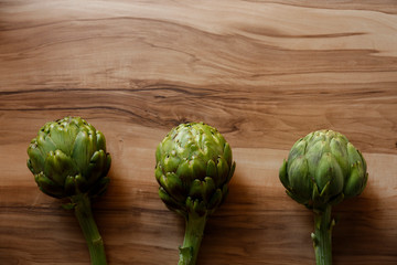 Fototapeta premium Fresh green Italian Artichoke natural wood background. Organic local produce vegetable on textured table. Vegan diet. Clean eating concept. Close up, top view, flat lay.