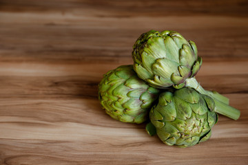 Fresh green Italian Artichoke natural wood background. Organic local produce vegetable on textured table. Vegan diet. Clean eating concept. Close up, top view, flat lay.
