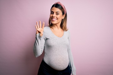 Young beautiful brunette woman pregnant expecting baby over isolated pink background showing and...