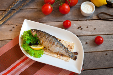Grilled trout fish with spices, herbs and lemon fried on a grill on a white plate, top view