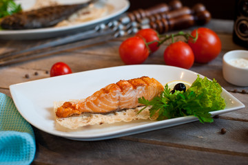 Grilled salmon steak served on a white plate with lemon and herbs. wooden background